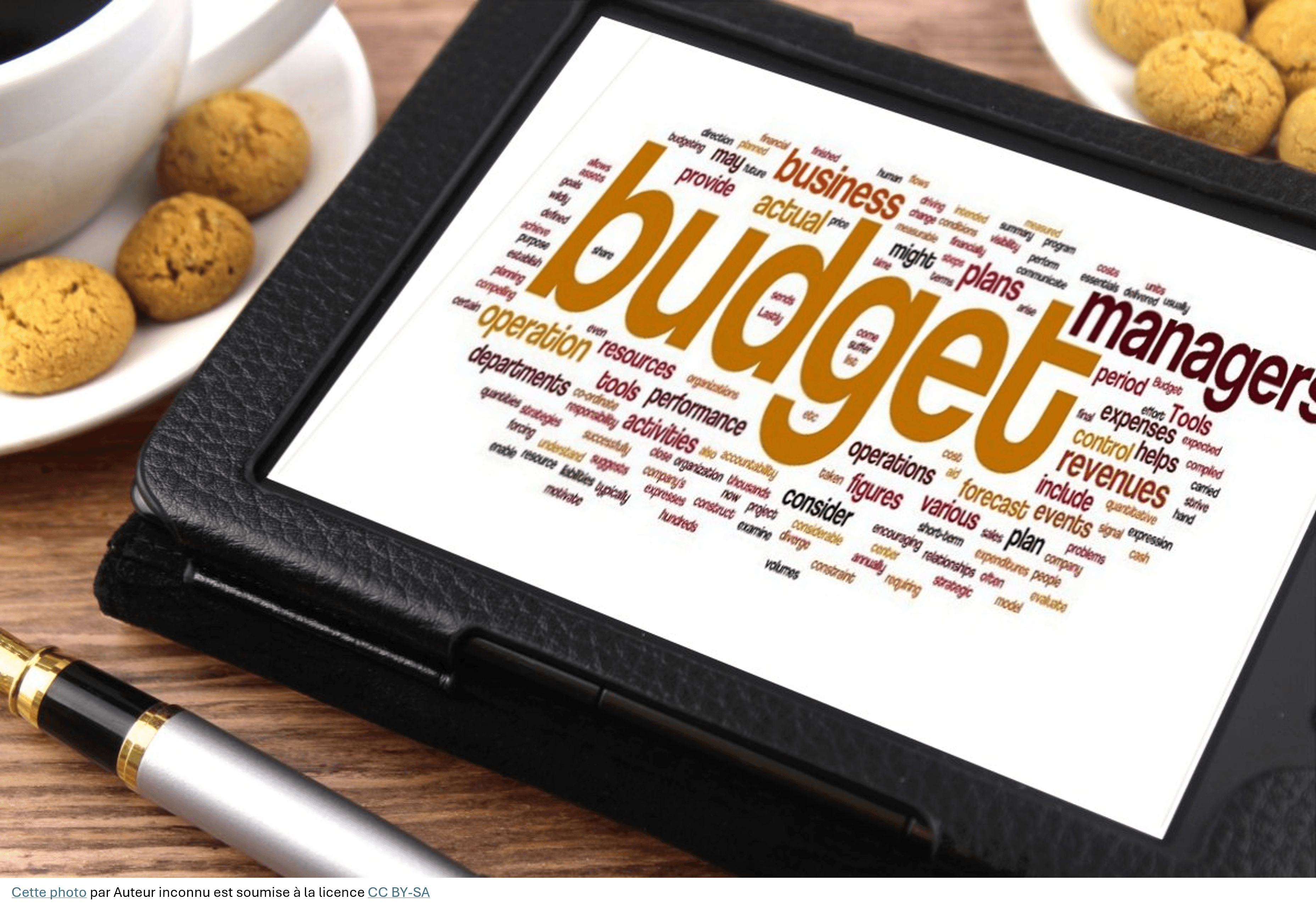 Tablette affichant un nuage de mots budget sur un bureau avec café et biscuits.